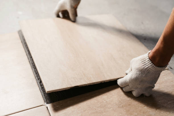 The hands of the tiler are laying the ceramic tile on the floor. Close up macro shot. Home renovation and building new house concept